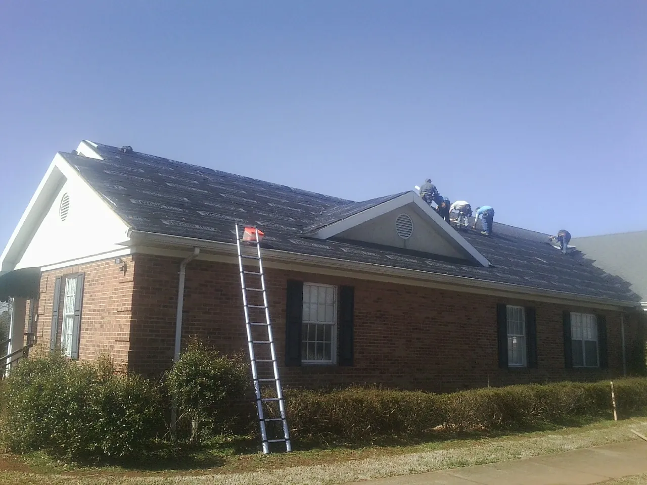 Crew tearing shingles off a brick ranch roof with a ladder set — Metal Roof Repair work by our crew in Seaside