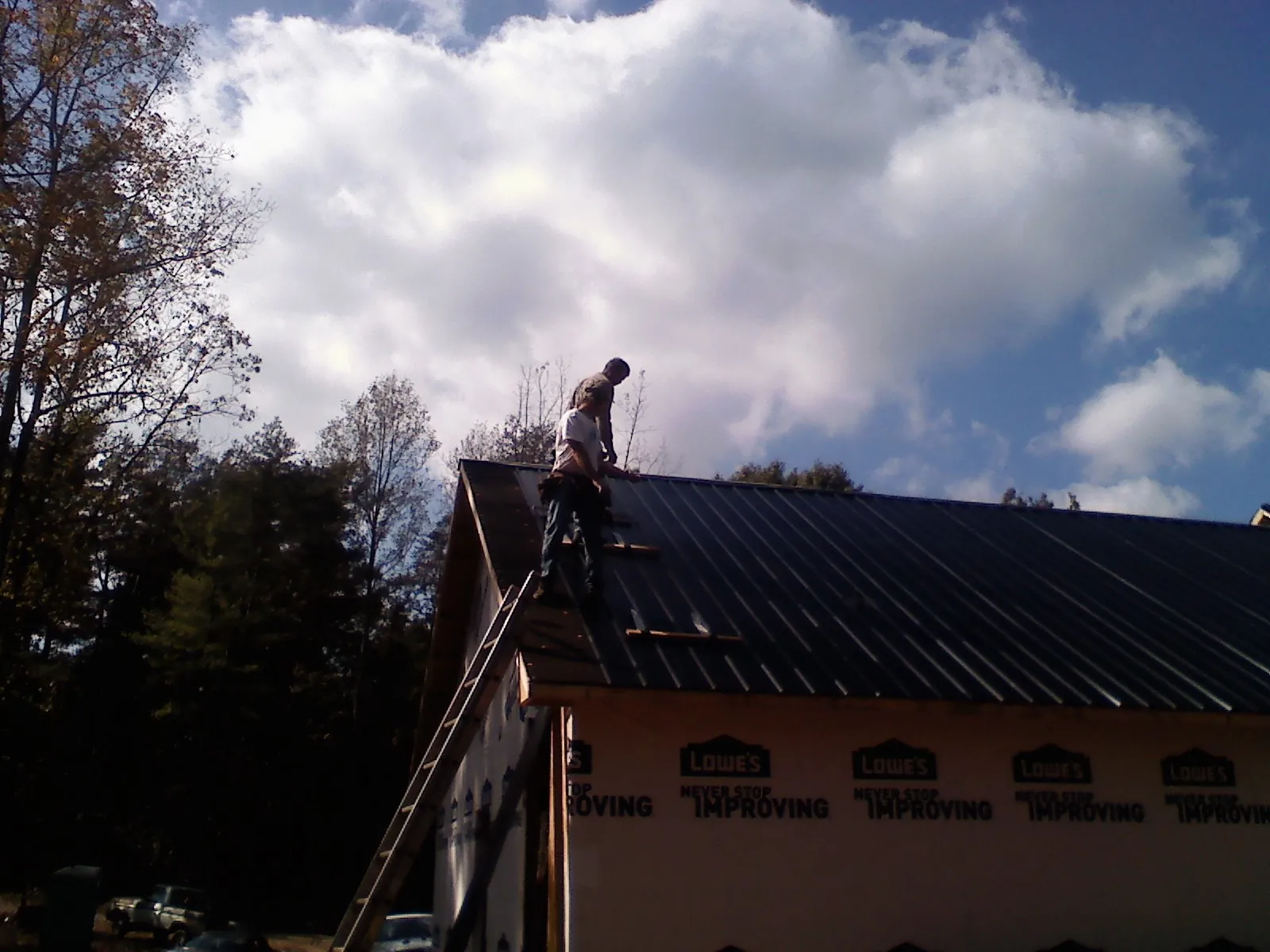 Roofer fastening dark metal panels high against a cloudy sky, from a Roof Inspection job in Seaside